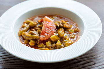 Close-Up of Traditional Okra Dish with Tomatoes on a White Plate on a Wooden Table
