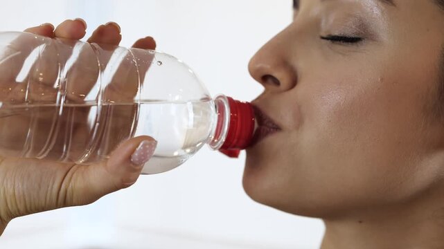 Young woman has workout at home during quarantine. Drinking water from bottle after training. Body hydration. Cut view and motion. Woman stop drinking.
