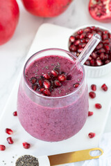 Pomegranate and chia seed smoothie in a glass with fresh fruit on white kitchen table.