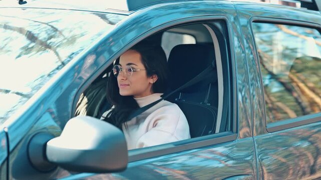 Young woman sit in car during travelling break. Girl in forest sitting inside and unbuckle the seat belt an open car's door to go outside. Happy positive girl on video.