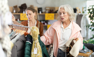 Two female clients near showcase examine goods, buying something winter warm outwear. Off line clothing store from retailer. Style and fashion type look, modern trends. Outlet, discount store