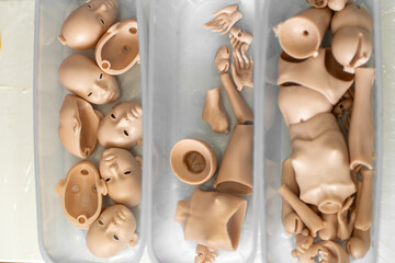 Closeup of silicone doll parts in containers, including faces, hands and body parts. Pieces are ready for assembly in the doll-making process