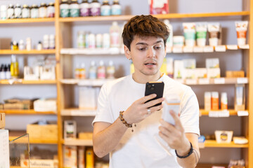 Guy scans the barcode of a package of food supplements in an eco supermarket on mobile phone. Buyer uses a QR code to read detailed instructions and information on how to use the dietary supplement
