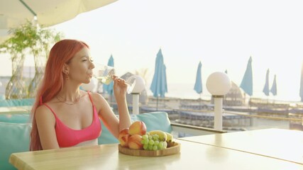 A woman enjoys a refreshing drink while sitting at a beachside resort during a beautiful summer sunrise over the sea