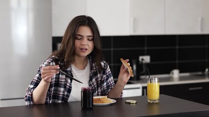 Young woman in kitchen during quarantine. Sit at table and put some jam on toast bread. Delicious breakfast in morning. - Powered by Adobe