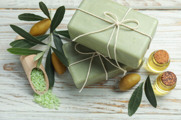 Natural soap bars with olives, sea salt, oil and green leaves on white wooden table, above view