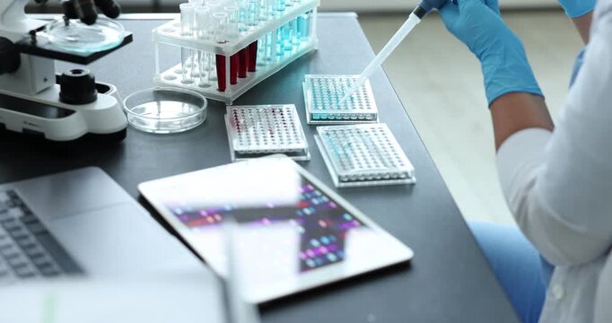 Research in genetics. Scientist with micropipette and microplate working at table in laboratory, closeup