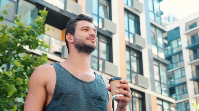 Young man exercising outside. Static video of guy drinking coffee or tea and have rest after workout, fitness or sport. Urban city view. Sporty guy take care obf body and health.
