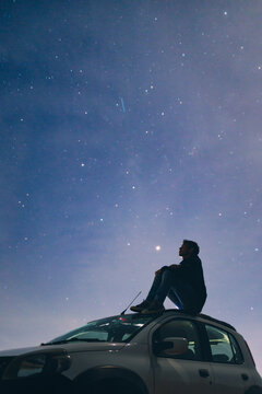 Traveler sitting on a car roof, gazing at the night sky, lost in deep thoughts and spiritual connection beneath the stars.