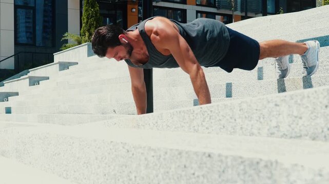 Young man exercising outside. Guy holding fet on steps and doing push up exercises. Training having workout outside on street. Camera moves forward.