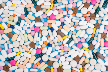Colorful assortment of various pills and capsules scattered on a blue background, showcasing different shapes, sizes, and colors, representing health and wellness concepts