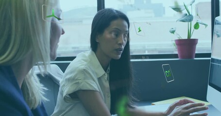 Dark-haired woman gesturing at monitor at desk, making green power-data icons pop for business demo - Powered by Adobe