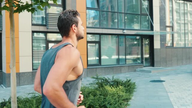 Young man exercising outside. Slow motion of guy's legs starting jogging or slow running on street near uran builing apartment. Man's feet in white sneakers in fast walking.