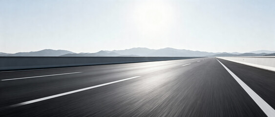A smooth asphalt road under bright sun with distant mountains in the background, creating a clear and open landscape.
