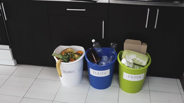 Young man in kitchen during quarantine. Video of three buckets for plastic, paper and organic waste. Srting and recycling process. Guy throw broccoli into orangic waste bucket.