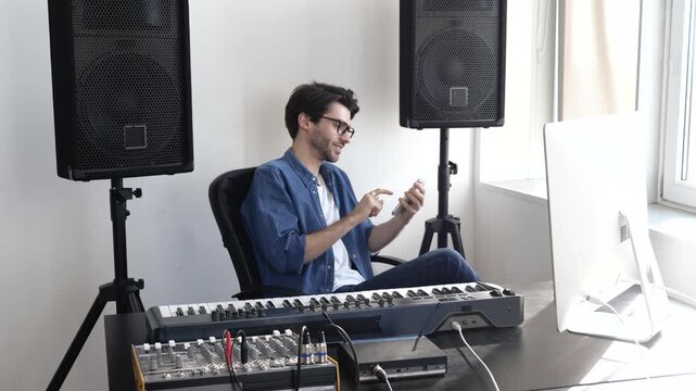 Young man in sound recording studio. Sitting at keyboard and typing on smartphone. Texting or sending message. Social media life.