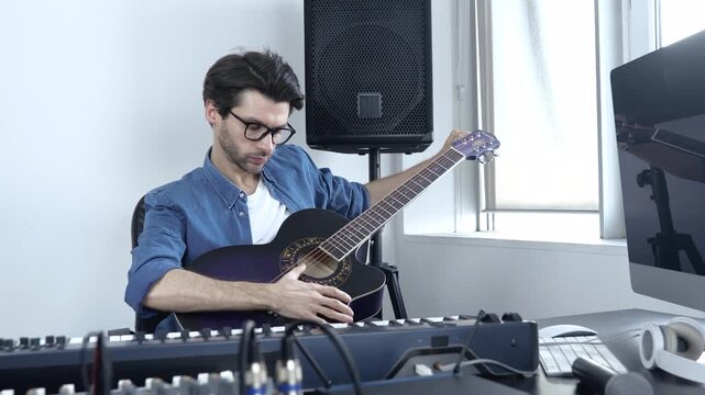 Young man in sound recording studio. Guy sit at table with mixing console on it and play on acoustic guitar. Recording sound alone in studio.