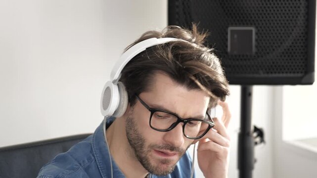 Young man in sound recording studio. Video portrait of guy listening to music through headphones and enjoy it. Rocking alone in room.