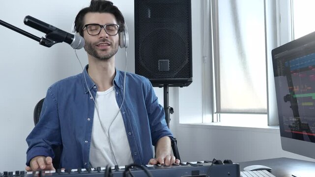 Young man in sound recording studio. Guy learning how to play on keyboard and sing. Non-profesional student learning. Enjoying process in slow motion.