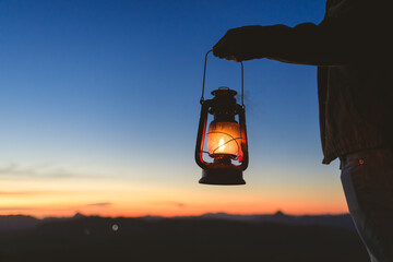 Hand holding a lantern at sunset, symbolizing faith, inner light, and spiritual reflection in a...