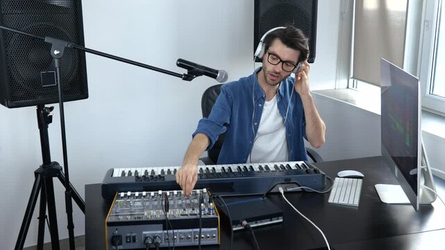Young man in sound recording studio. Guy in slow motion adjusting music mixing console and listening to it in headphones.