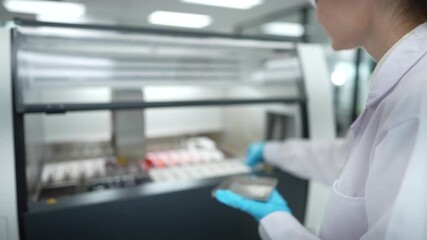 In a modern lab, a female scientist uses a tablet to monitor a large automated machine as it processes biological samples, combining human oversight with technological efficiency. - Powered by Adobe