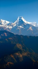 Majestic snow-capped peaks pierce a clear blue sky above rugged, forested mountain slopes bathed in warm sunlight.