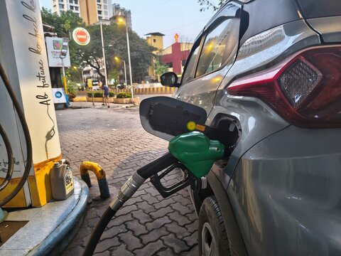 Close-up view of a car refueling at a petrol pump in an urban Indian city. Green fuel nozzle inserted in the vehicle tank, symbolizing rising fuel prices, transportation, and energy consumption.