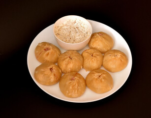 Buuzy, traditional Buryat dish steamed with sour cream sauce in a round plate on a black background.