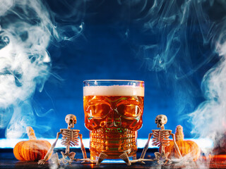 Halloween beer glass on blue smoky background, skeletons with pumpkins