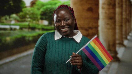 Woman holding rainbow flag on city street celebrating lgbt pride with joyful expression against outdoor urban backdrop. - Powered by Adobe