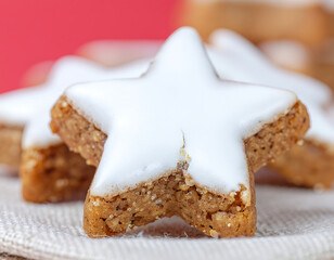 Close-up of star-shaped Zimtsterne cookies with white icing on a white surface against a red background.