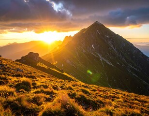 Fototapeta premium Golden sunset illuminates a majestic mountain peak, casting warm hues across the grassy slopes.
