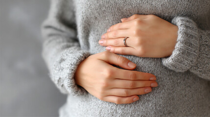 Close-up of a young pregnant Asian woman’s hands gently resting on her exposed belly, expressing love, connection, and anticipation of motherhood in soft natural light.