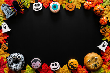 Halloween party decorations with cute macarons, donut, cookie and maple leaves on black background for Halloween holiday concept.