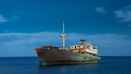 Rusty Shipwreck Resting in Calm Blue Sea at Night