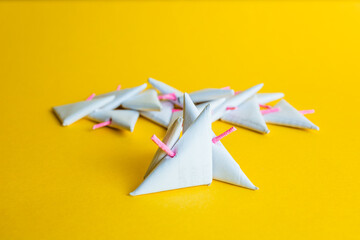 Low-angle shot of a group of white paper triangular-shaped firecrackers, with prominent pink fuses against a vibrant yellow background.