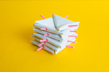 Close-up of a geometric stack of several white paper triangular firecrackers with pink fuses, on a vibrant yellow studio background.