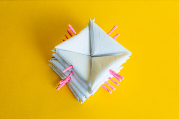 Close-up of a geometric stack of several white paper triangular firecrackers with pink fuses, on a vibrant yellow studio background.