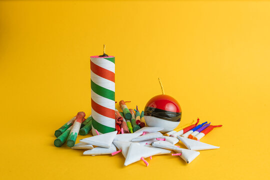  Composition of a variety of festive pyrotechnics, including rockets, a sphere, and triangular firecrackers, on a vibrant yellow background.