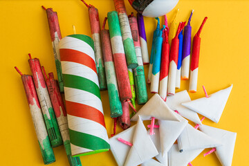 Top-down view of a variety of bright, colorful explosives and firecrackers laid out on a striking yellow studio background.