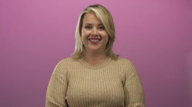 Young blonde woman with direct gaze speaking with lips open in a pink studio; confidence empowerment.