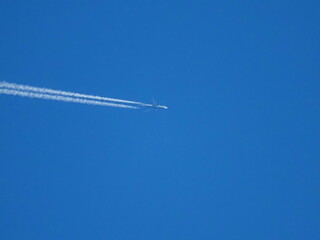 Airplane flying high in blue sky leaving white contrail trail