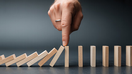 Hand stopping domino effect, preventing a chain reaction of falling blocks