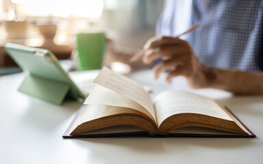 select focus on open book and blurred person in background using digital tablet to seek knowledge via internet online