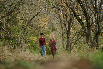 Fototapeta premium A candid portrait of a young couple walking along a quiet autumn woodland path, capturing genuine connection, warm tones and relaxed natural interaction with subtle authenticity.