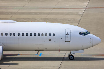 Close-up view of a commercial airplane cockpit and nose section at an airport. A pilot is preparing for flight, representing the aviation and travel industry.