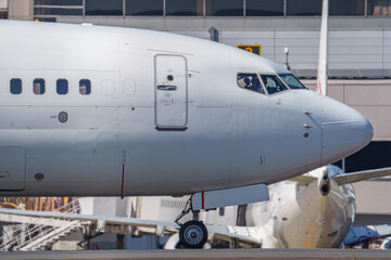 Close-up view of a commercial airplane cockpit and nose section at an airport. A pilot is preparing for flight, representing the aviation and travel industry.