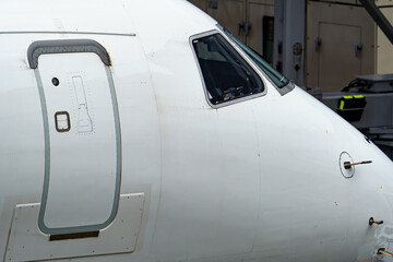 Close-up view of a commercial airplane cockpit and nose section at an airport. A pilot is preparing for flight, representing the aviation and travel industry.
