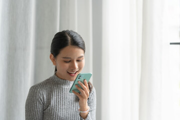 Asian woman using voice assistant on smartphone at home conversation with online assistant Voice chat bot conversational AI Modern Technologies.